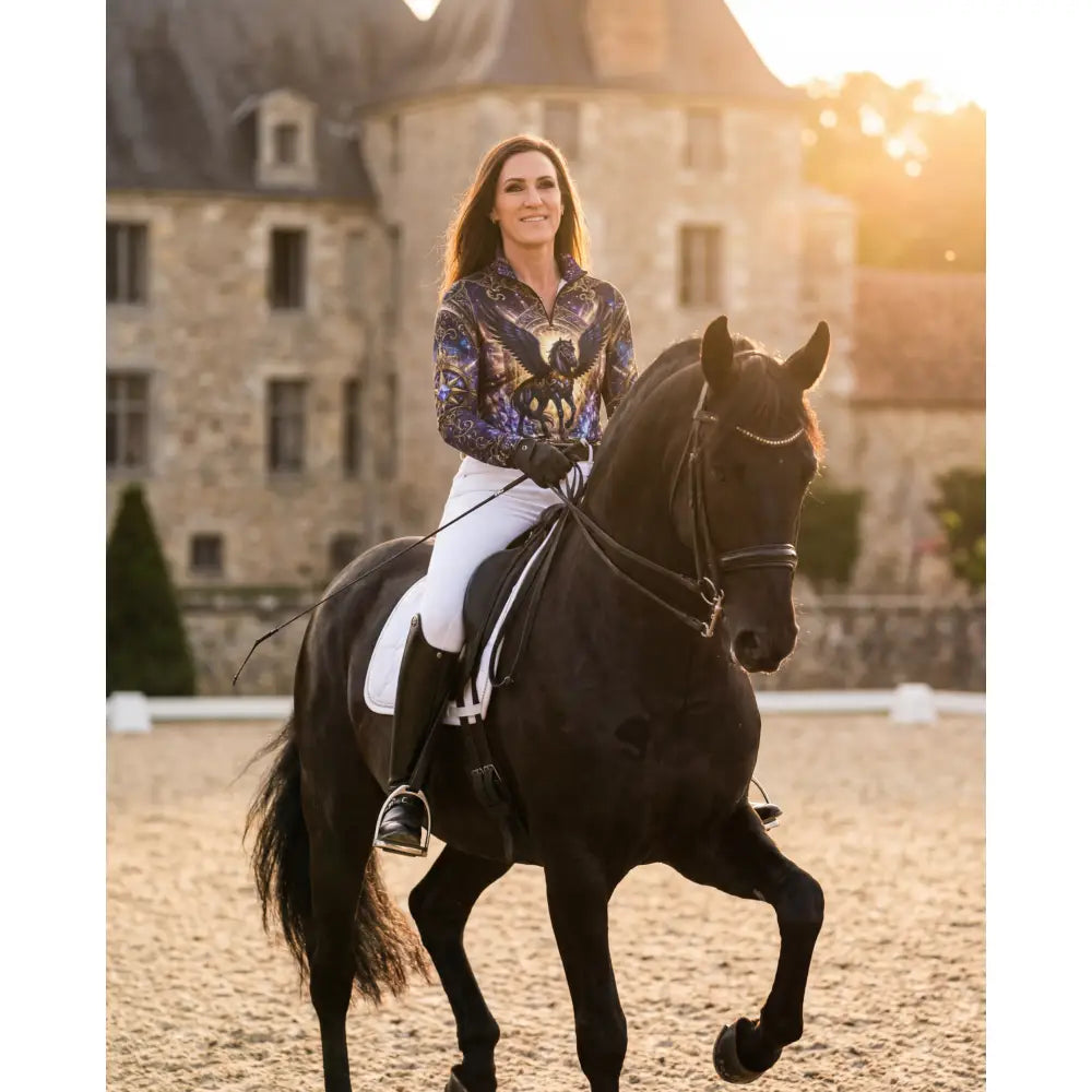 A woman rides a sleek black horse wearing an astral ascension performance equestrian sun shirt with cosmic winged design