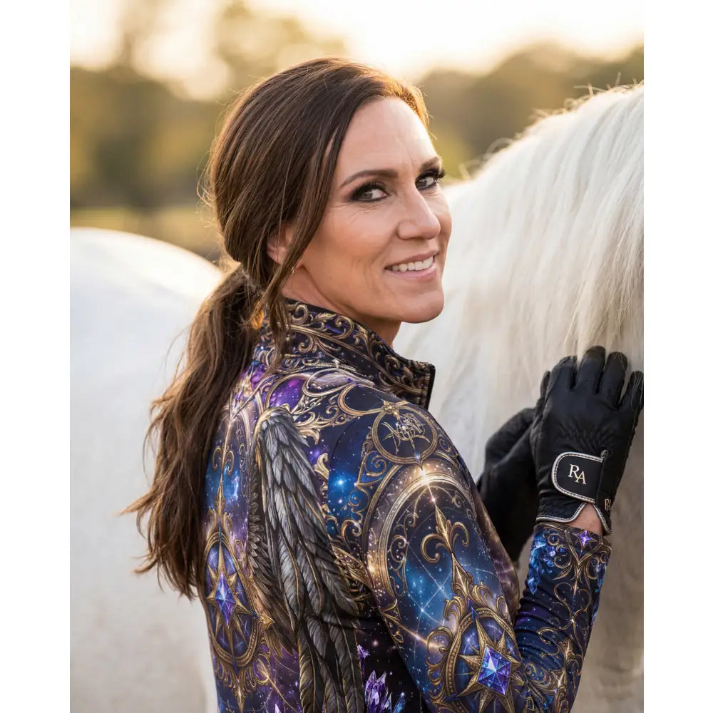 A woman wearing a long-sleeved astral ascension performance equestrian sun shirt with cosmic winged horse print in purple and gold