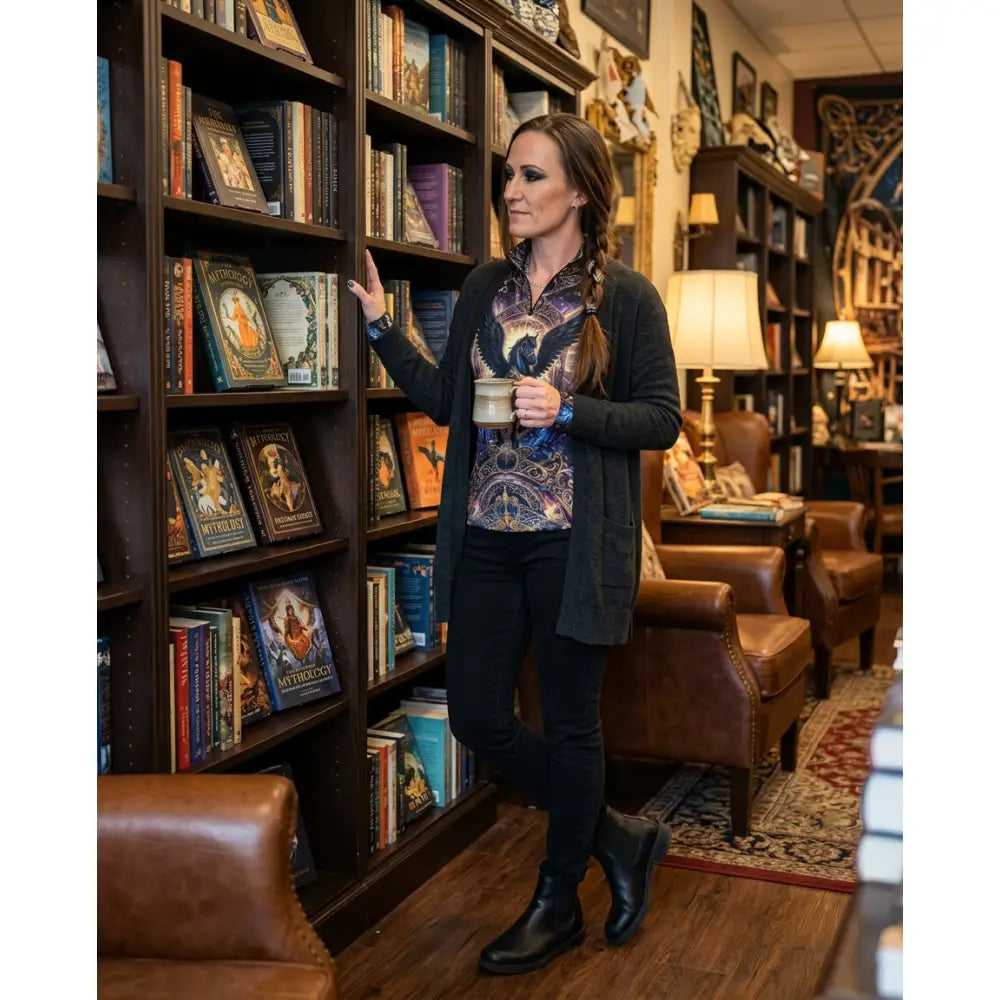 Woman wearing astral ascension black equestrian sun shirt with cosmic winged horse print paired with black pants and boots