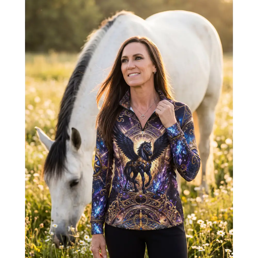 A woman wears a long-sleeved full-zip astral ascension performance equestrian sun shirt with a black winged horse design