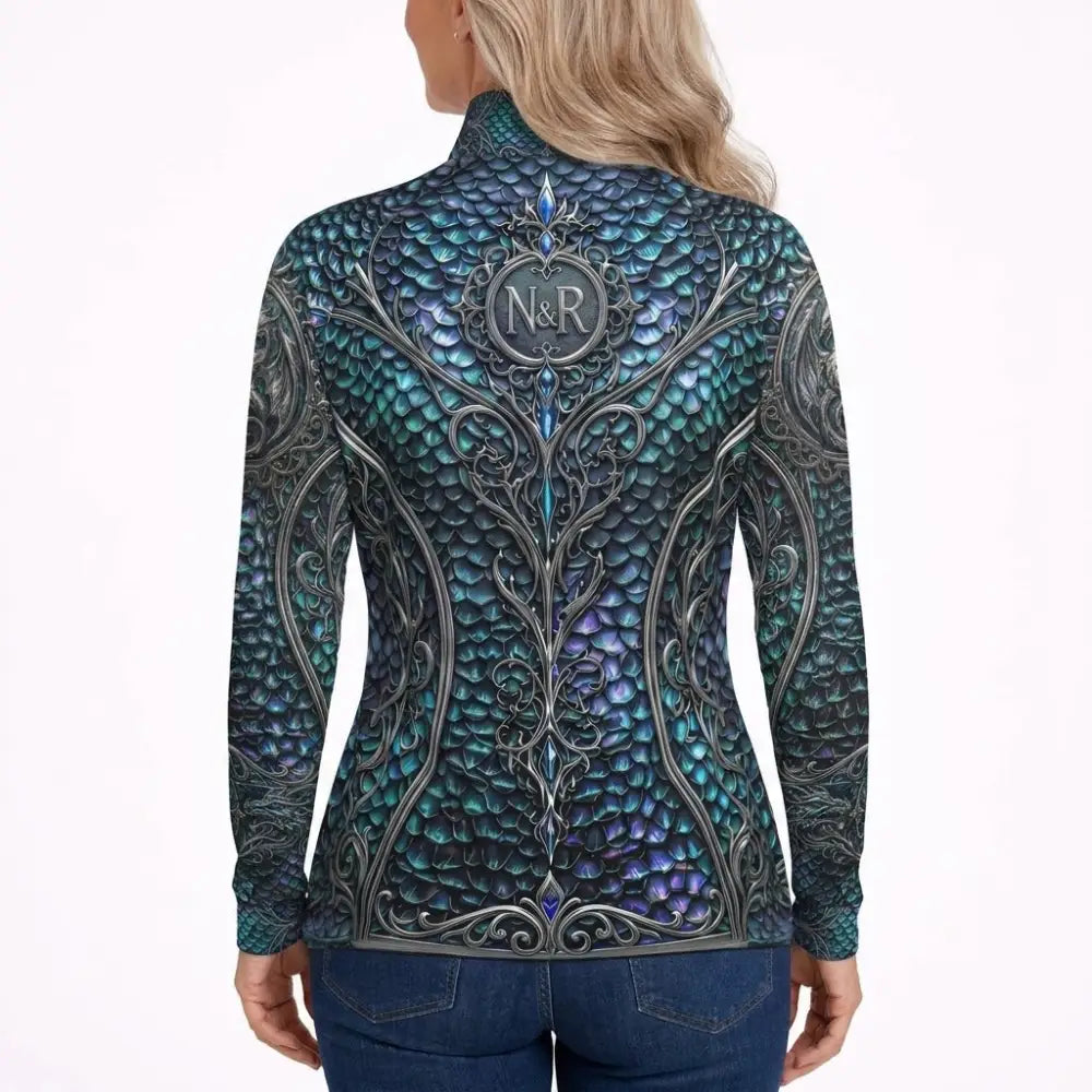 A woman wears a teal and purple dragon-scale patterned long-sleeved performance equestrian sun shirt with silver details