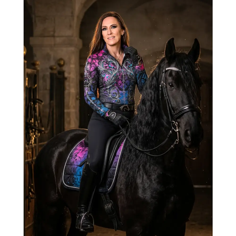 A woman wears a vibrant purple and blue floral long-sleeved midnight radiance performance equestrian sun shirt upf50+ riding a black horse