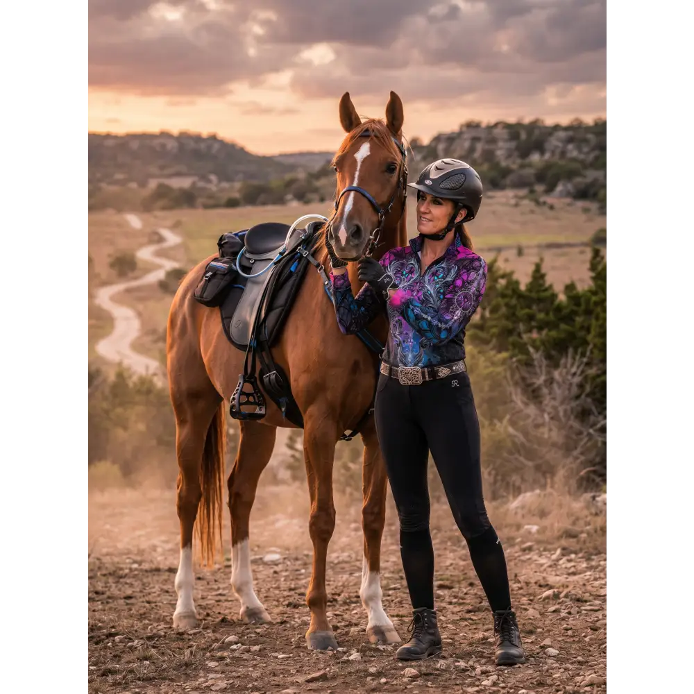 A woman wearing a vibrant purple and blue patterned midnight radiance performance equestrian sun shirt upf50+ stands beside a chestnut horse