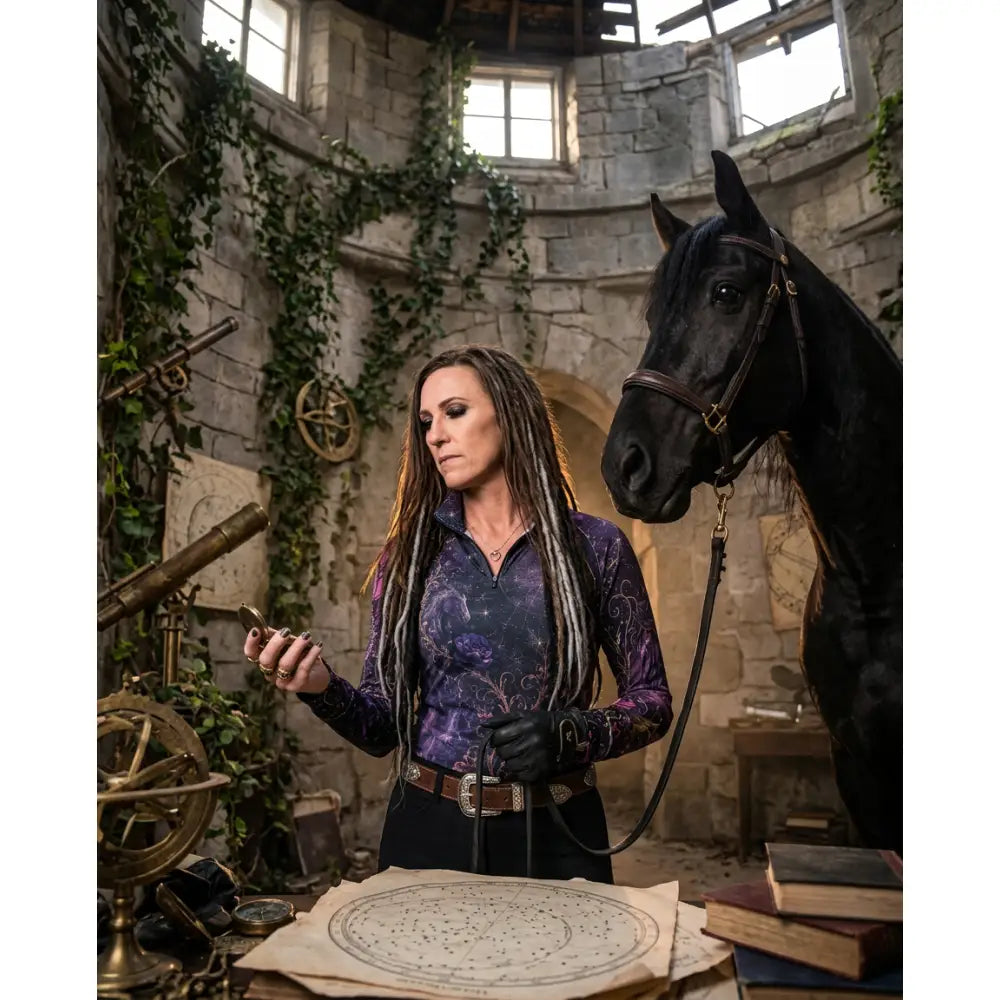 A woman wearing a purple and black galaxy patterned long-sleeved moonthorn nocturne equestrian sun shirt by karen reinertson