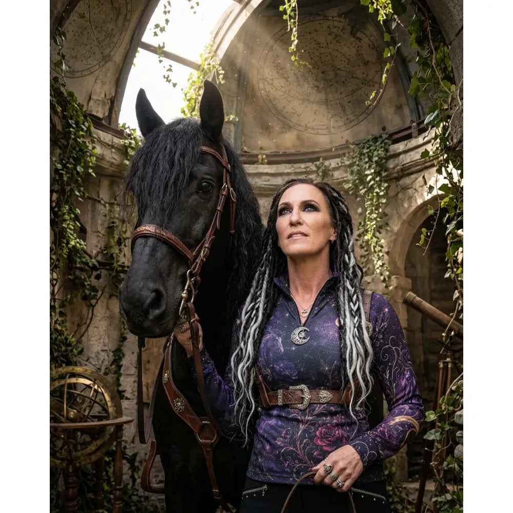 A woman with braided silver and black hair wears a purple blue moonthorn nocturne celestial print UPF50+ equestrian sun shirt by karen reinertson