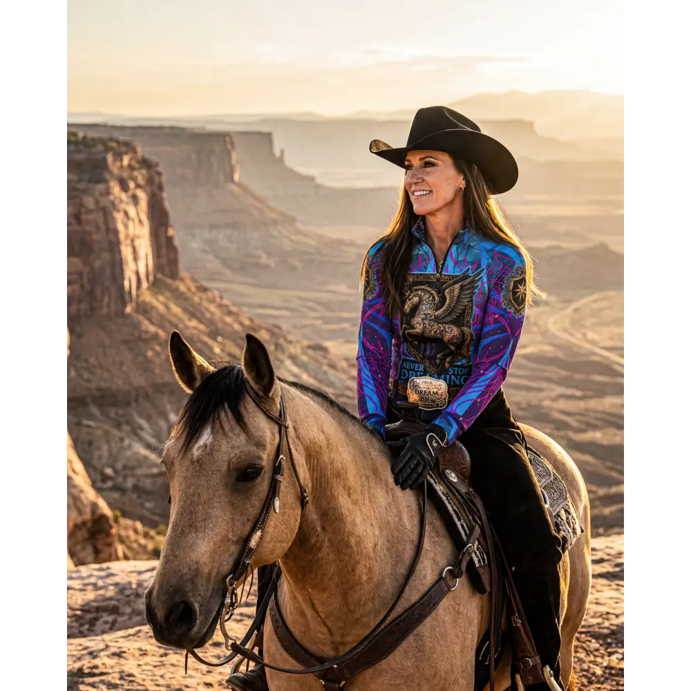 A woman wears a vibrant blue purple patterned never stop dreaming performance equestrian sun shirt upf50+ while riding a horse
