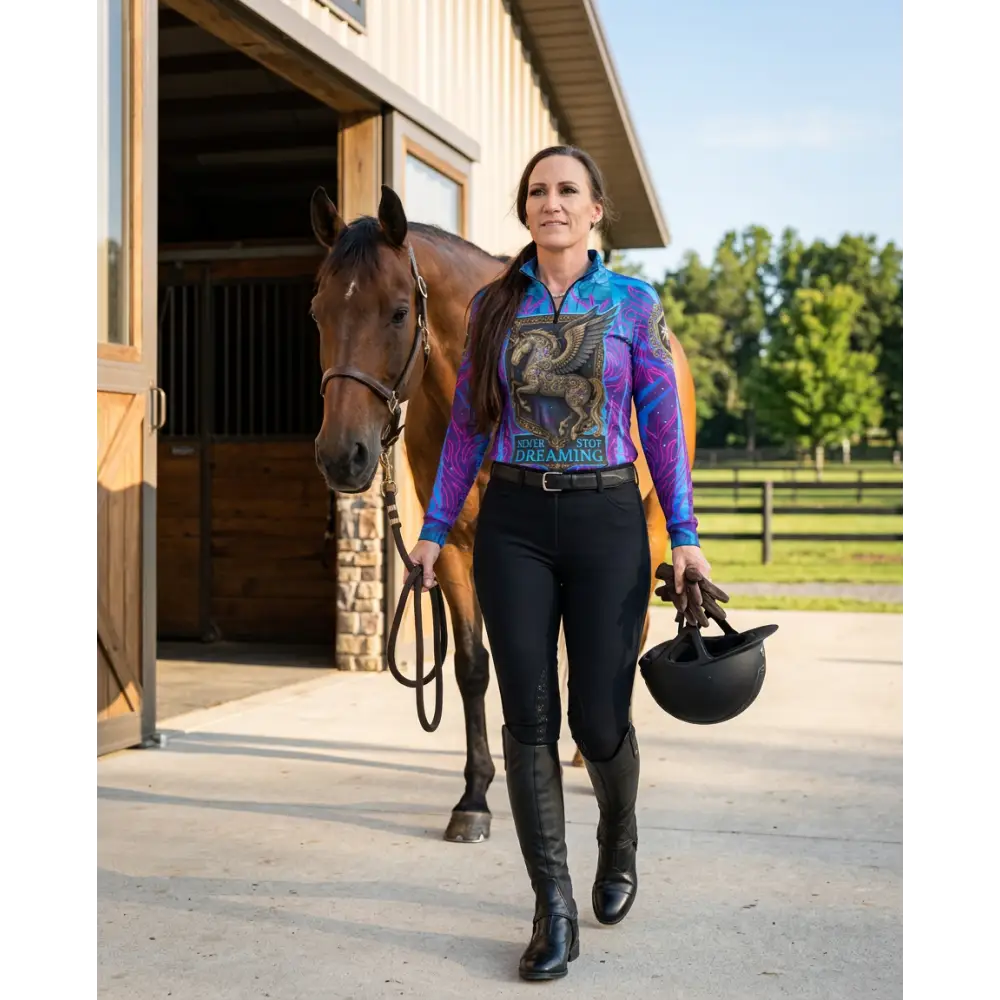 A woman wears a vibrant long-sleeved performance equestrian sun shirt with pegasus graphic and never stop dreaming print