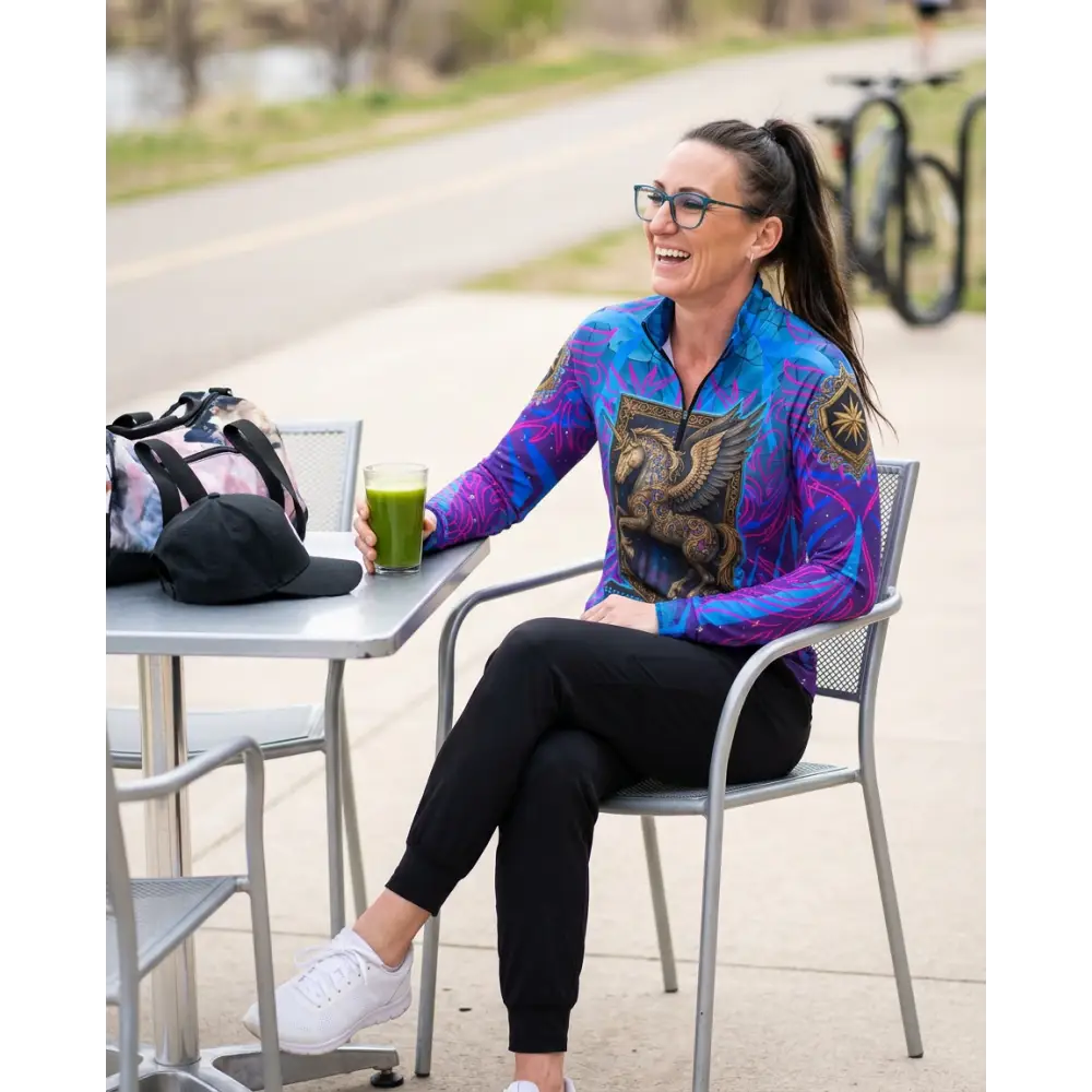 Woman wearing a vibrant blue and purple long-sleeved performance equestrian sun shirt with golden griffin design and UPF50+ protection