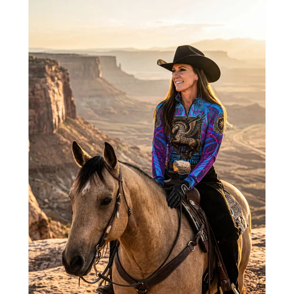 A woman wears a vibrant blue and purple winged horse performance equestrian sun shirt while riding a tan horse in a canyon