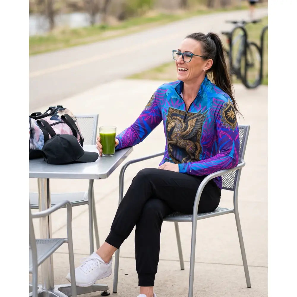 Woman wearing a vibrant blue and purple equestrian sun shirt with golden griffin design performance equestrian sun