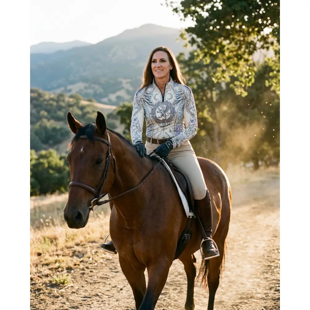 A woman wearing a white and blue panthera arcana equestrian sun shirt with arcane wing and scale floral embroidery by karen reinertson