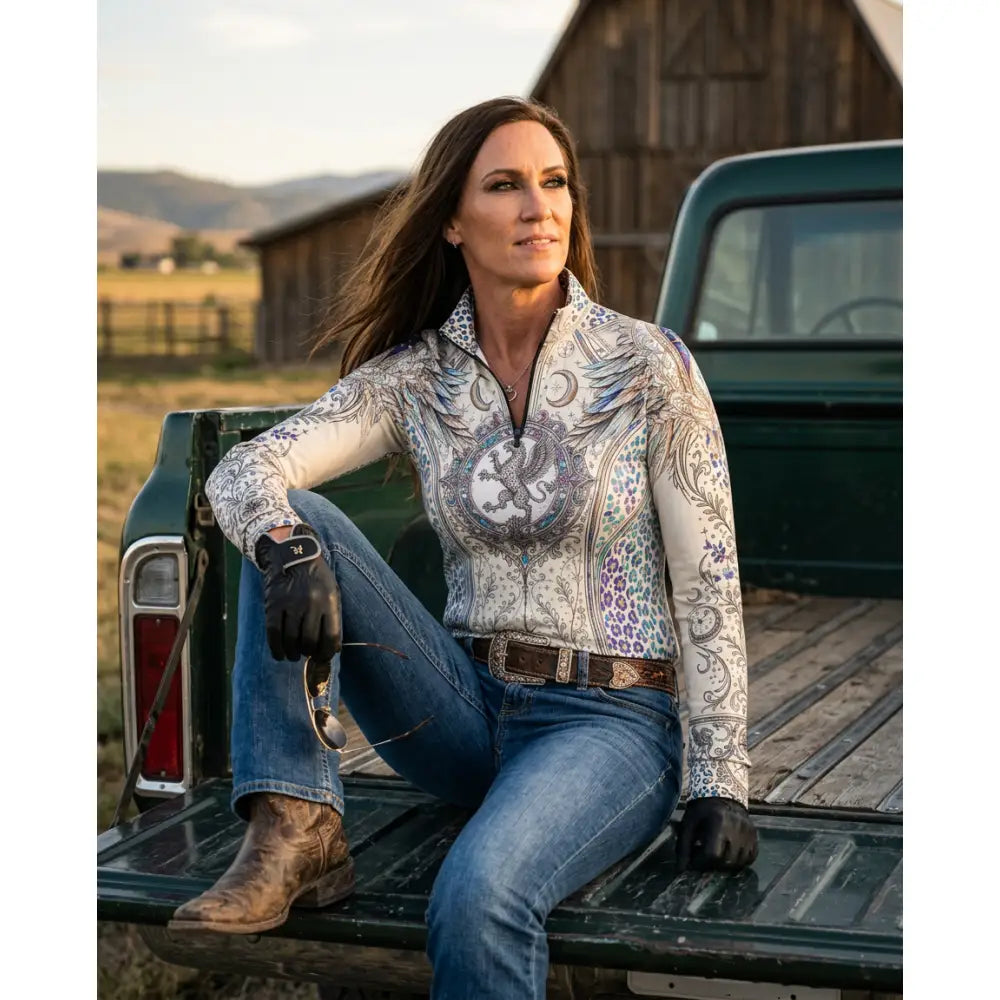 A woman wearing a white long-sleeved pantera arcana equestrian sun shirt with arcane wing and scale embroidery by karen reinertson