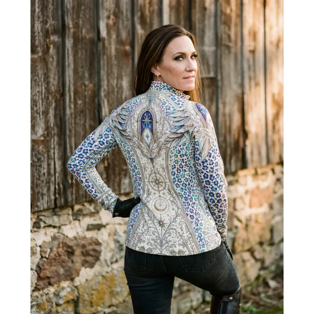 A woman wearing a panthera arcana equestrian sun shirt by karen reinertson with arcane wing scale print in blue gray and white
