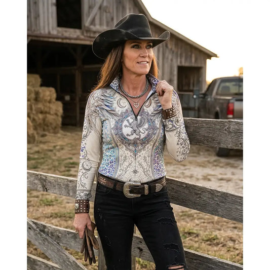 A woman wears a cream western-style pantera arcana equestrian sun shirt with blue gray dragon embroidery by karen reinertson