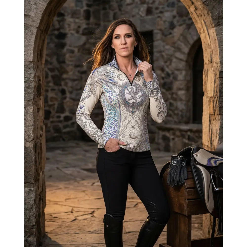A woman wearing a panthera arcana equestrian sun shirt with arcane wing and scale print in shades of gray blue and white