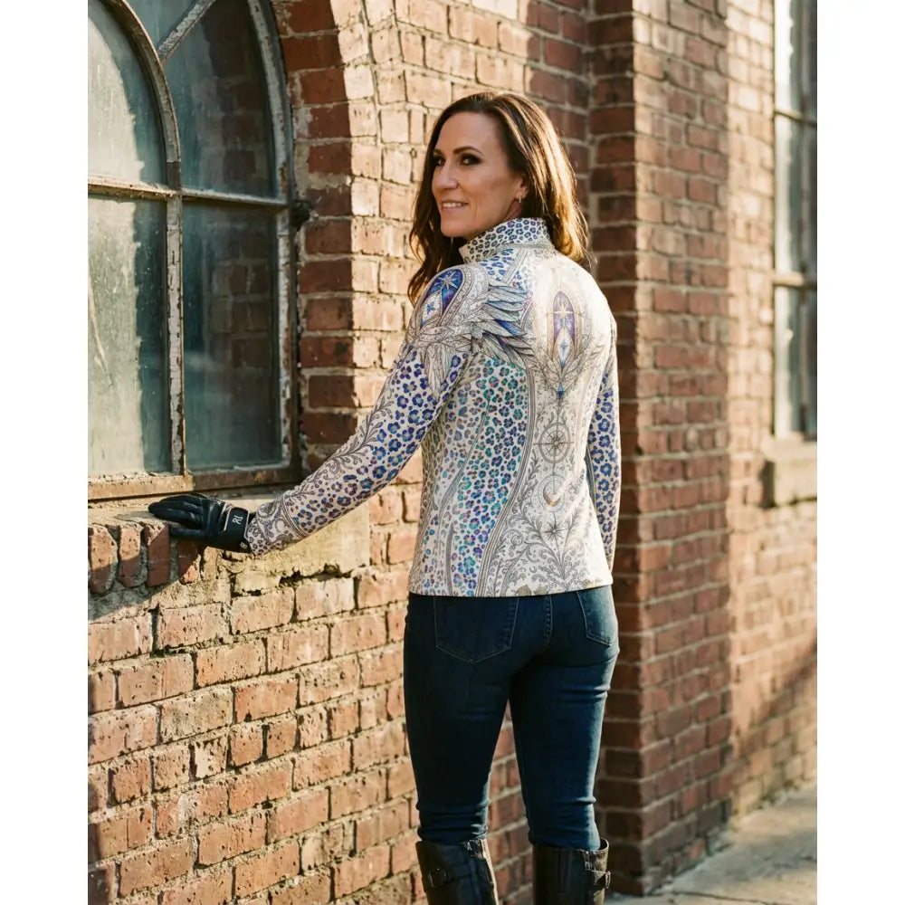 A woman wears a panthera arcana equestrian sun shirt by karen reinertson with arcane wing and scale blue gray print