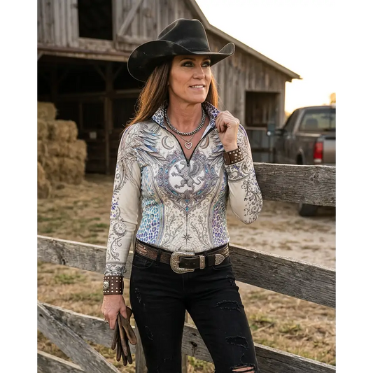 A woman wears a cream-colored panthera arcana upf50+ equestrian sun shirt with blue and gray dragon embroidery