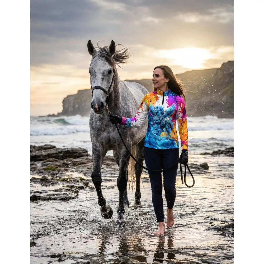 A woman walks barefoot with her grey horse wearing a vibrant tie-dye riptide radiance equestrian sun shirt