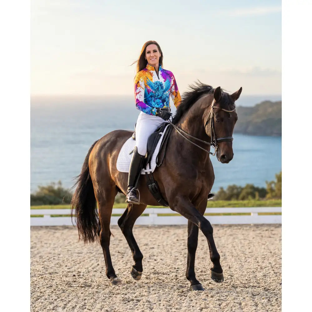 A woman rides a dark brown horse wearing riptide radiance pegasus ocean print upf50+ equestrian sun shirt from ripley signature collection