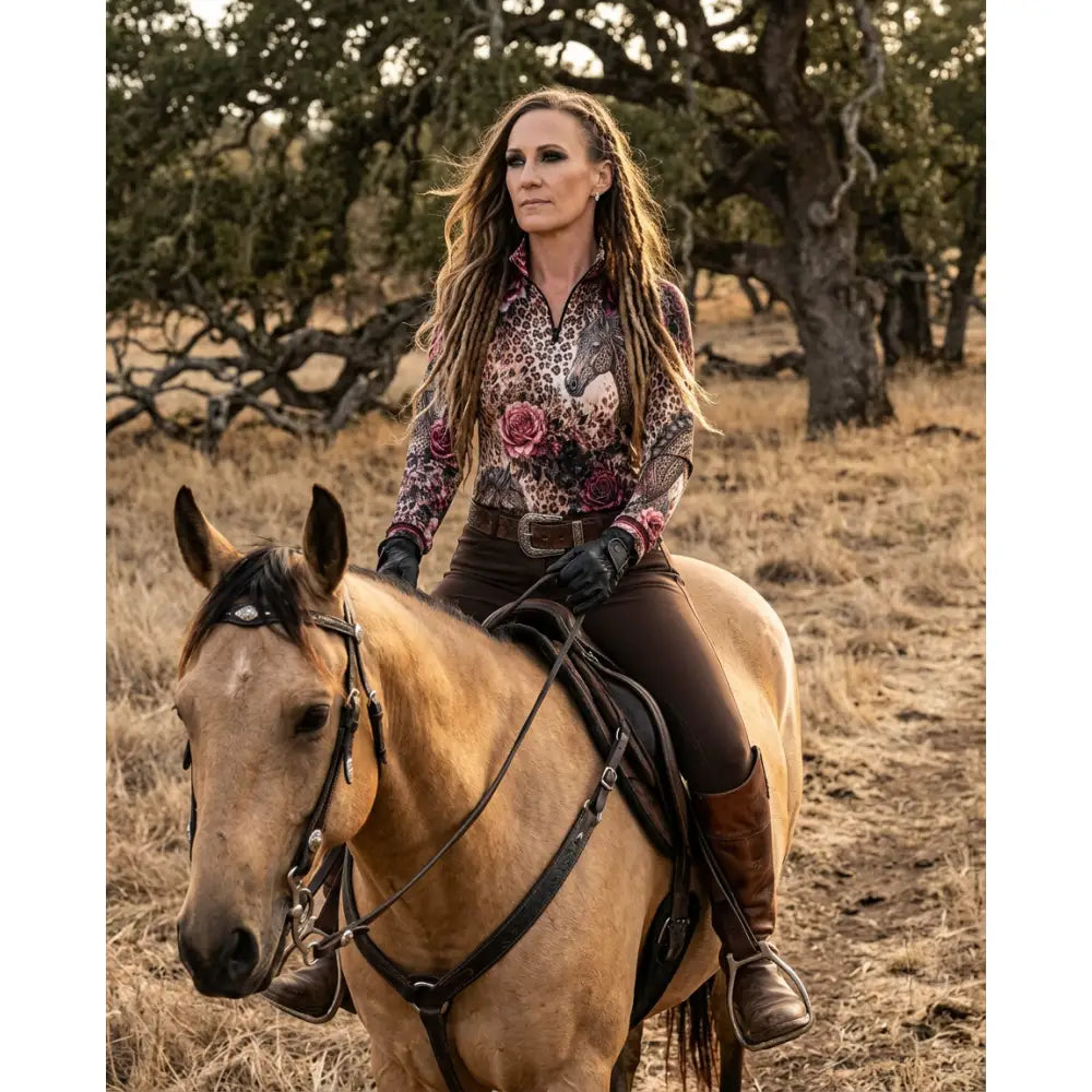 A woman wearing karen reinertson rosae equiferus leopard rose equestrian sun shirt rides a light brown horse