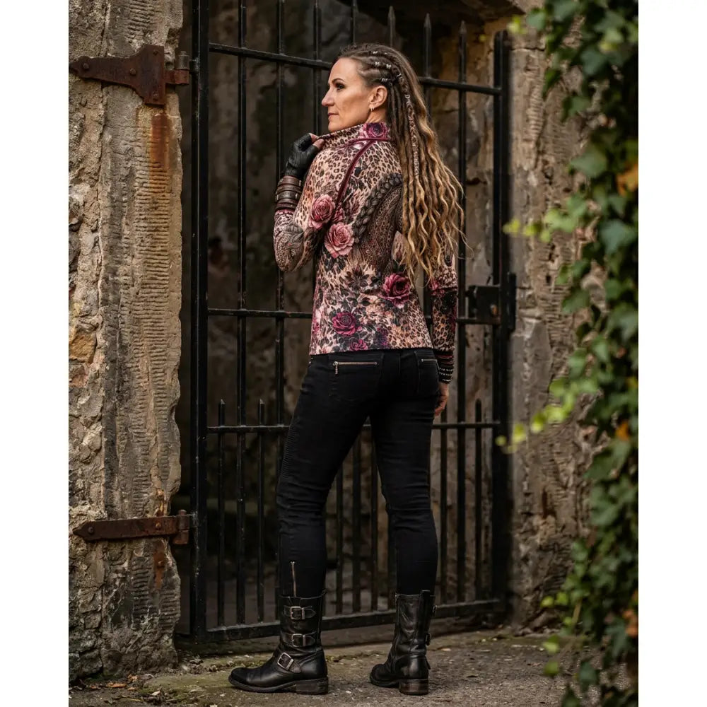 A woman wears a rosae equiferus equestrian sun shirt with leopard print, embroidered pink roses, black jeans, and boots