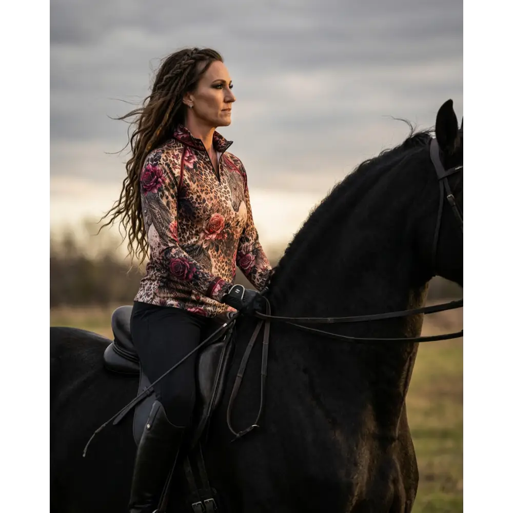 A woman rides a black horse wearing a rosae equiferus long-sleeved floral leopard print upf50+ equestrian sun shirt