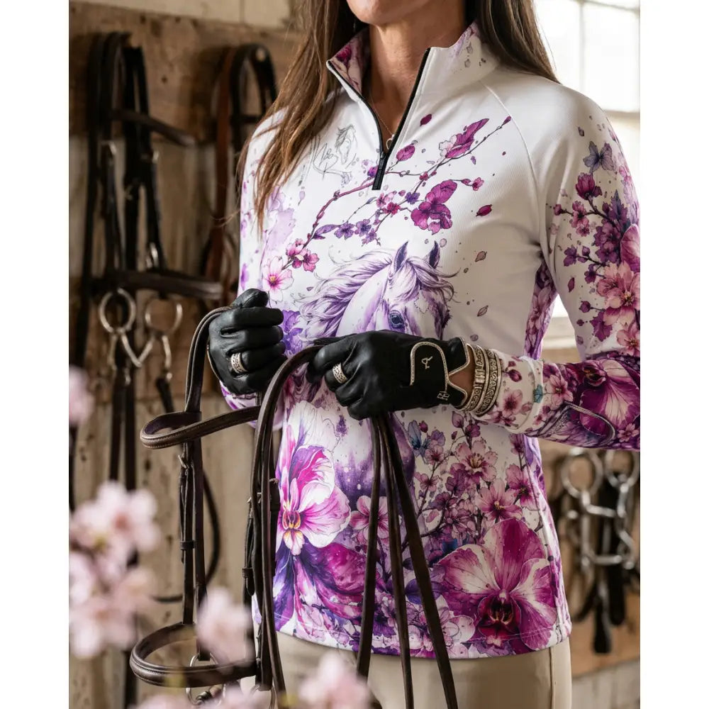 A woman wearing a sakura wildheart white long-sleeved upf50 equestrian sun shirt with orchid cherry blossom horse print by karen reinertson