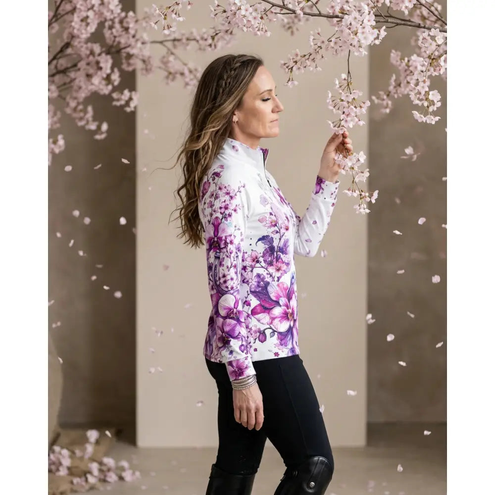 A woman wearing a sakura wildheart long-sleeved white zip-up equestrian sun shirt with orchid and cherry blossom prints by karen reinertson