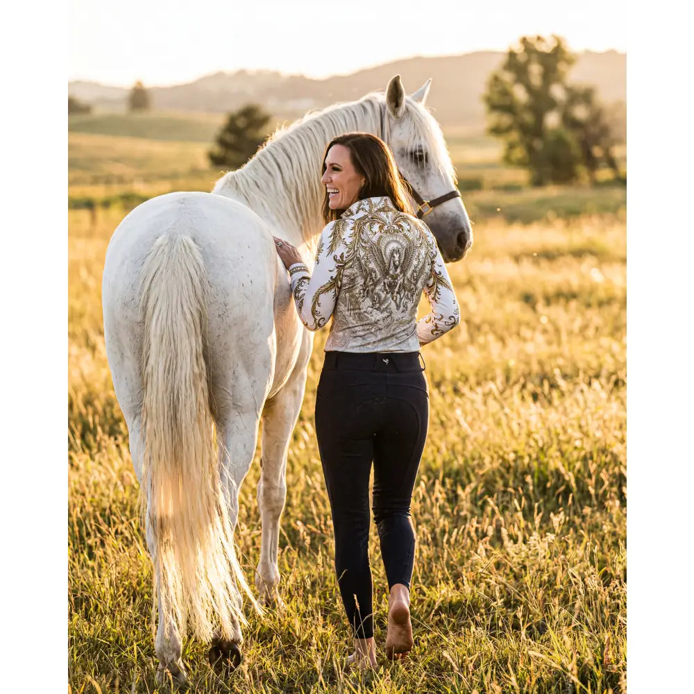 A woman wears the solis aeternum wearable art sun shirt from ripley signature collection with a white horse in a field