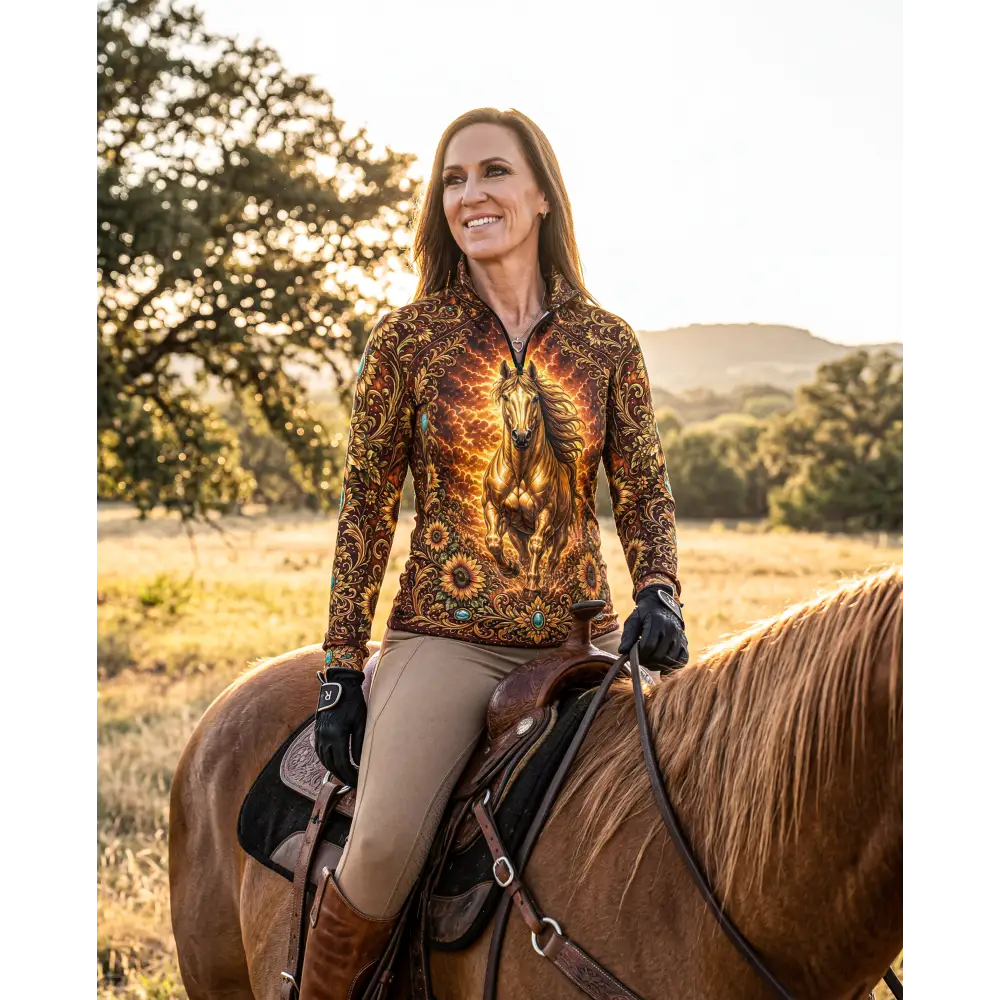 A woman wears a long-sleeved sunfire sovereign performance equestrian sun shirt with a golden horse design and fiery patterns