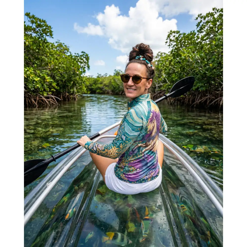 Transparent kayak with silver frame and black paddle paired with tidewoven reefborn ocean reef print wearable art shirt