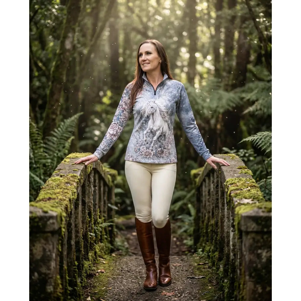 A woman wears a soft blue-gray unicornis caelestis equestrian sun shirt with a white horse and floral pattern by karen reinertson