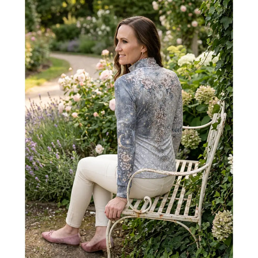 A woman wearing a unicornis caelestis equestrian sun shirt by karen reinertson in muted gray with floral and celestial print