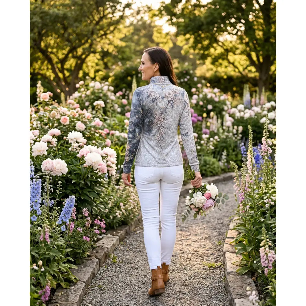 A woman wears a unicornis caelestis equestrian sun shirt by karen reinertson with a floral pattern and upf50+ protection