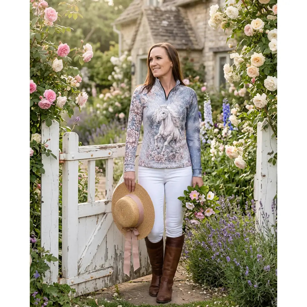 A woman wears a unicornis caelestis equestrian sun shirt with a white horse print and floral pattern by karen reinertson