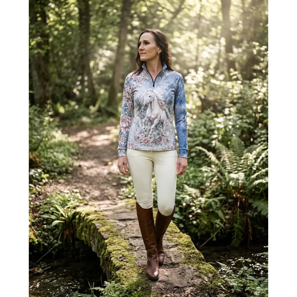 A woman wears a soft blue unicornis caelestis equestrian sun shirt with a white horse print by karen reinertson