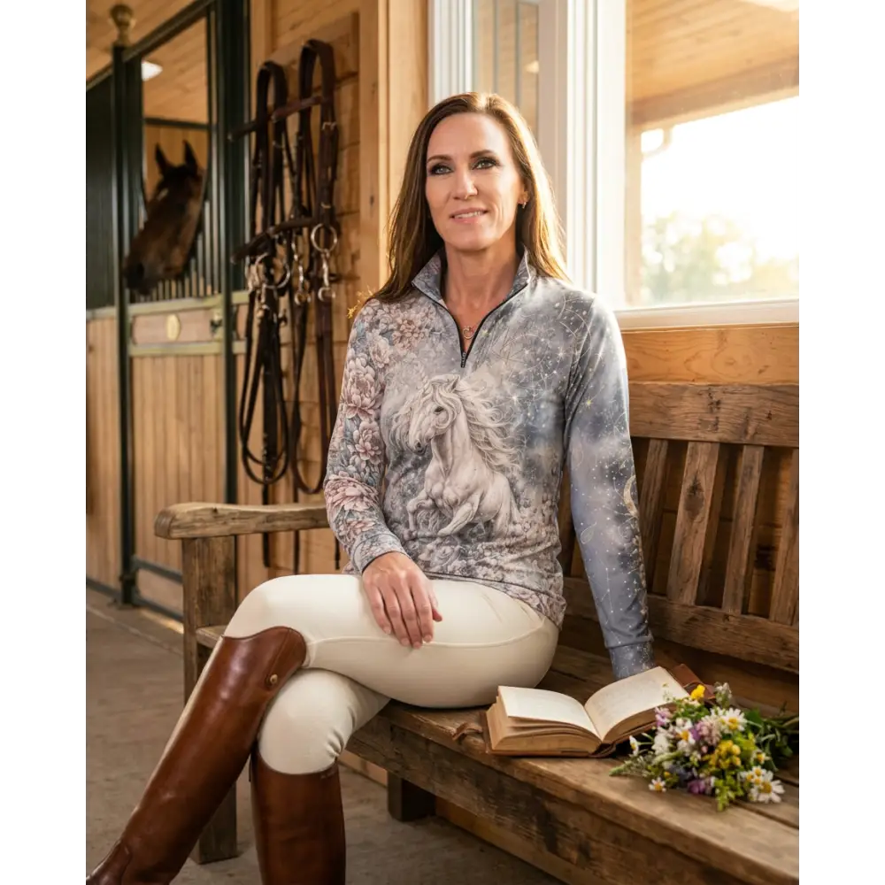 A woman wearing a long-sleeved unicornis caelestis performance equestrian sun shirt with a white horse print and upf50+ protection