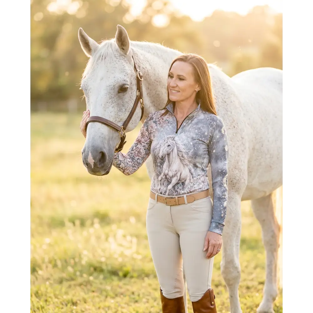 A woman wearing a gray and white horse print unicornis caelestis performance equestrian sun shirt with UPF50+ protection