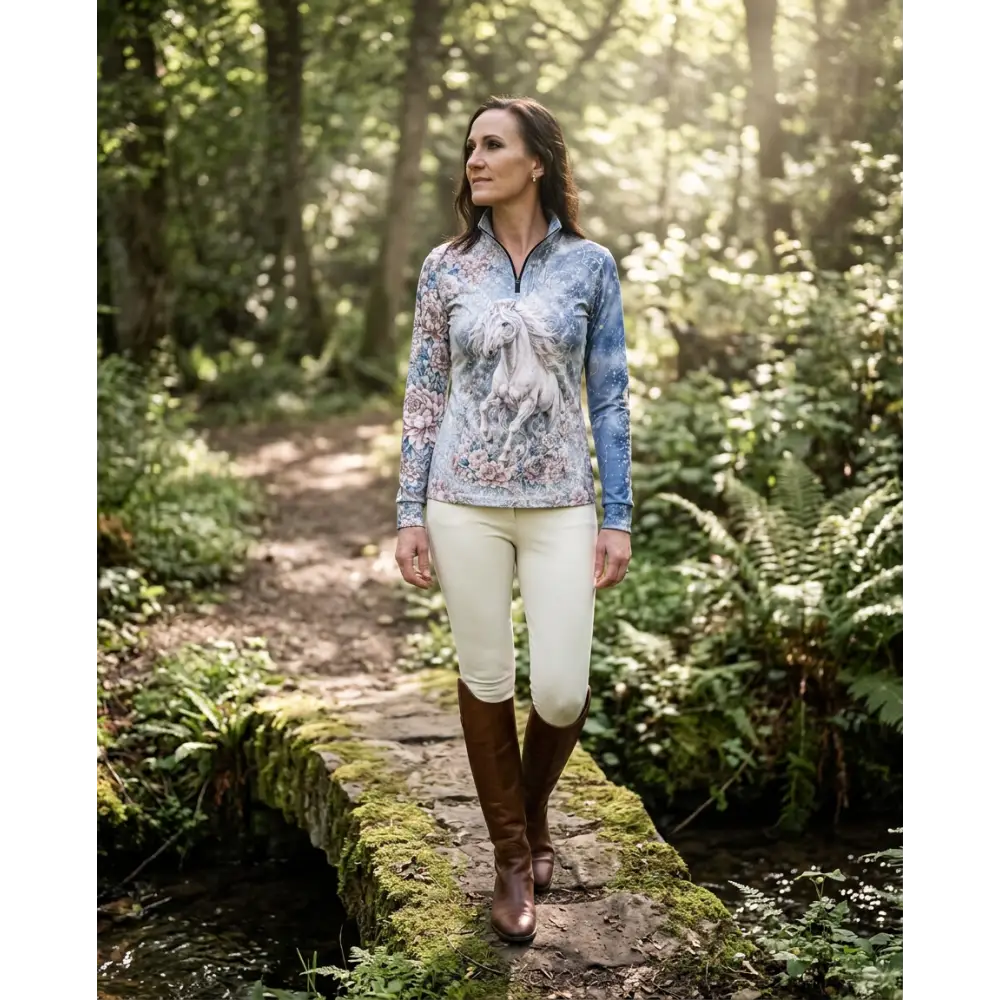 A woman wears a soft blue unicornis caelestis performance equestrian sun shirt with white horse design and upf50+ protection