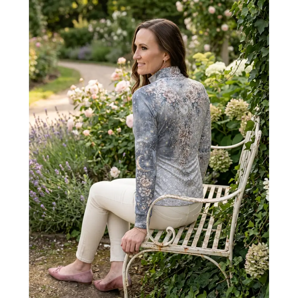 A woman wearing a muted gray unicornis caelestis performance equestrian sun shirt with floral celestial pattern and upf50