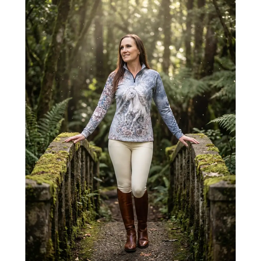 A woman wears a soft blue-gray unicornis caelestis performance equestrian sun shirt with white horse floral pattern