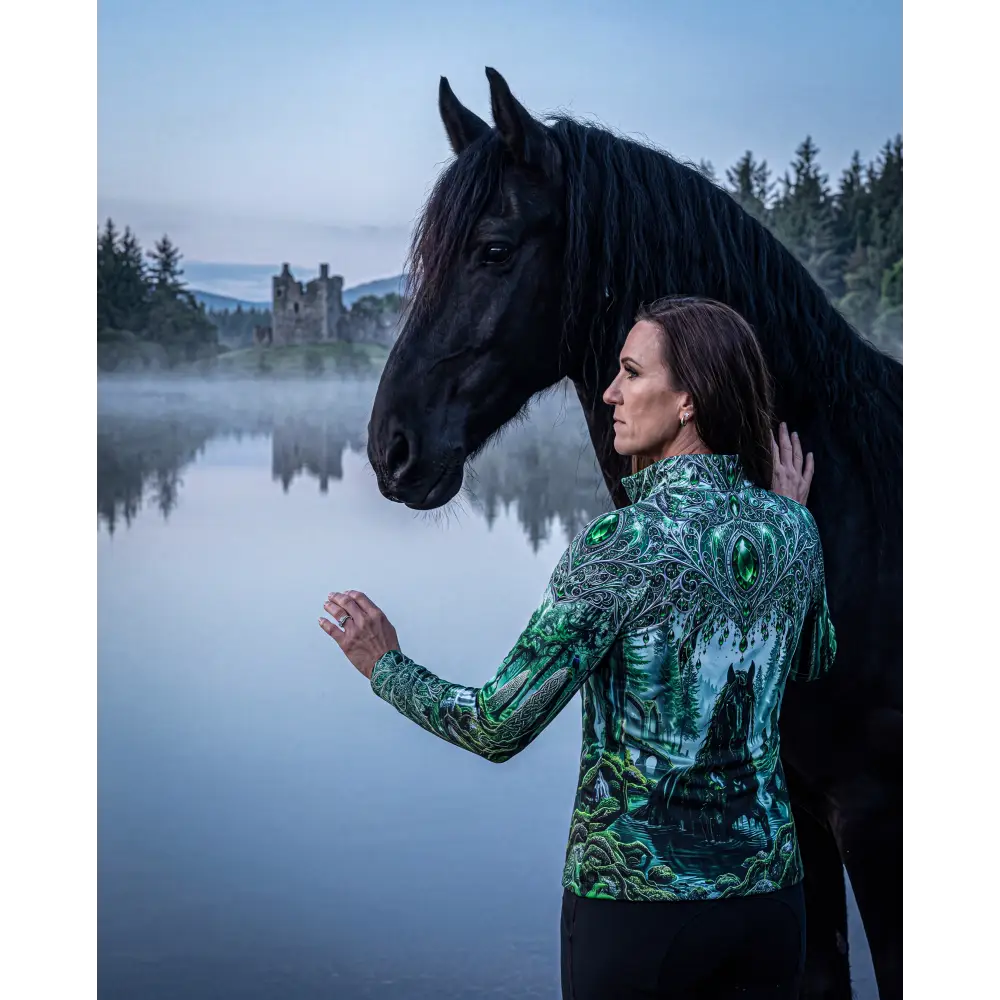 A woman wears a whispering waters performance equestrian sun shirt with green black forest design and upf50 plus protection